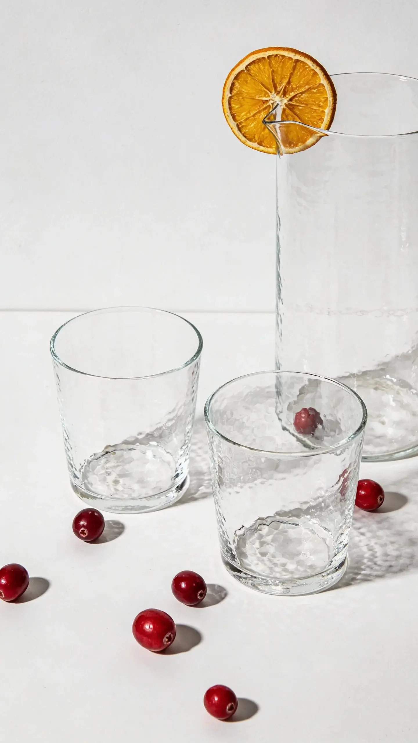 Minimalist scene: pitcher and glassware with cranberries, citrus slice