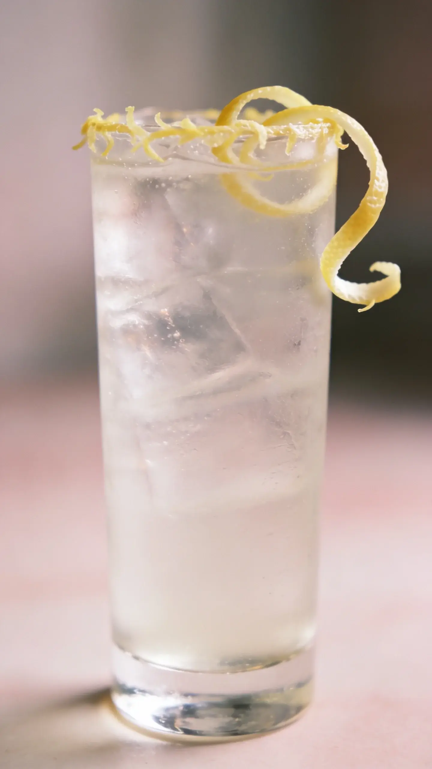 Tall highball glass, lemon zest garnish, soft pastel backdrop