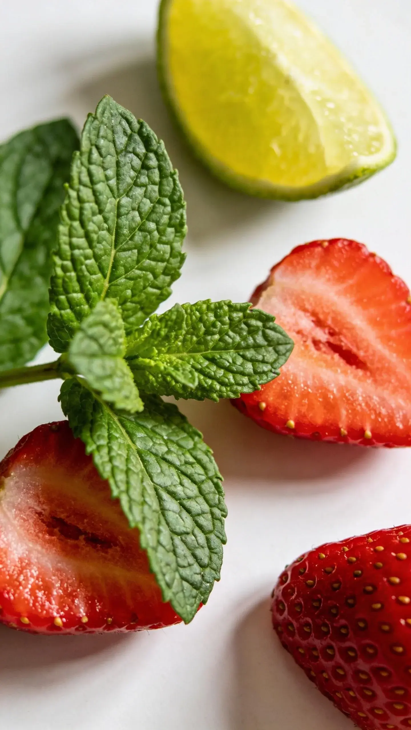Fresh mint leaves beside sliced strawberries, lime wedge